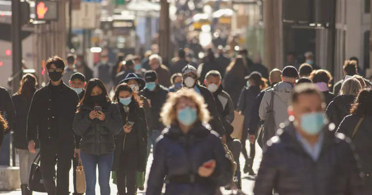 Lots of people wearing masks, walking down a street in New York City.