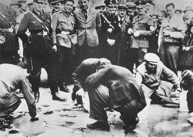 Soldiers mock as men crouch to scrub a Viennese footpath.