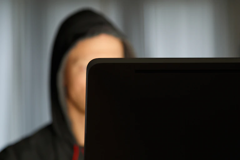 A hooded, blurred out figure is seen looking at a computer