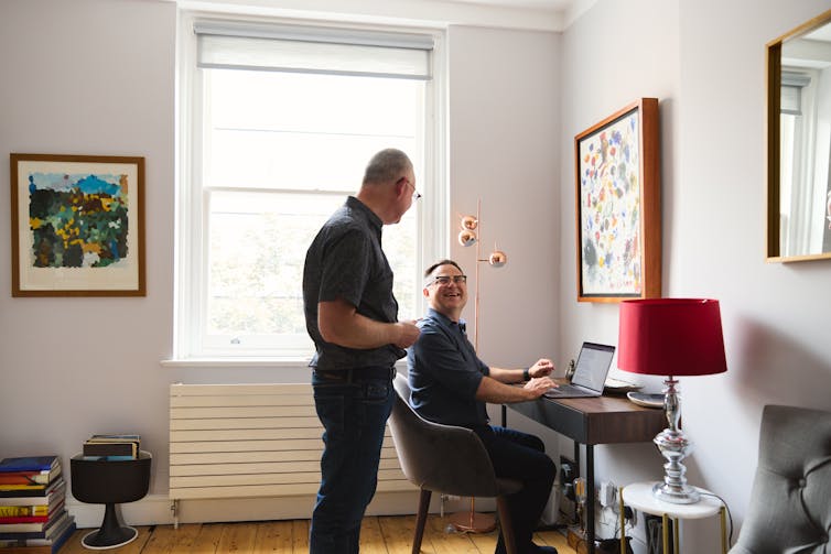 One man, working in a home office, talking happily to another man.