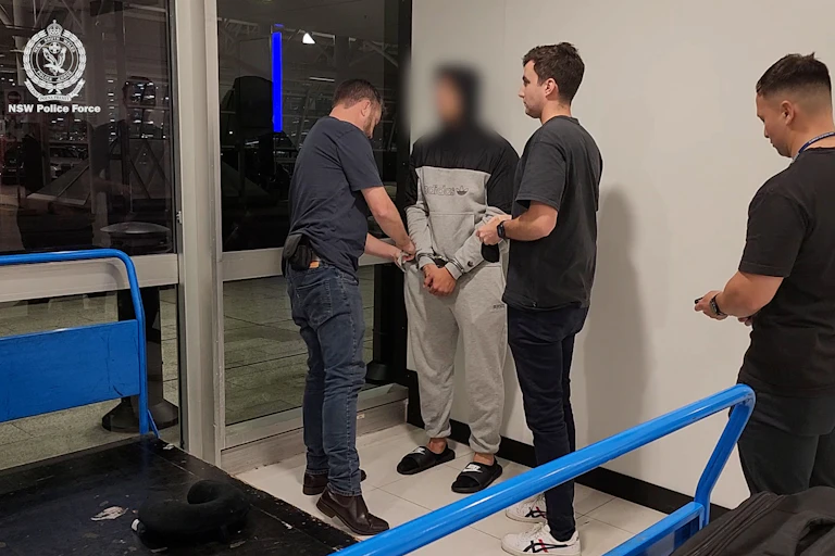 A man in a tracksuit with his face blurred out is handcuffed