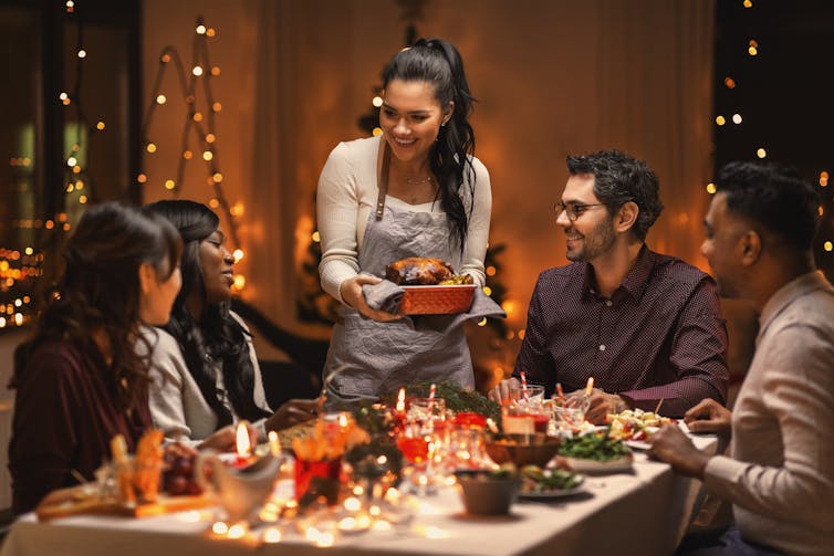 Standing woman holding a plate of food alongside table of seated people
