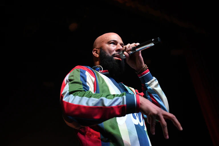 Bald bearded Black man wearing colorful shirt raps into a microphone.