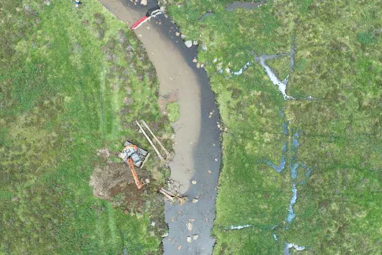aerial shot of grey river, green banks and digger on riverside