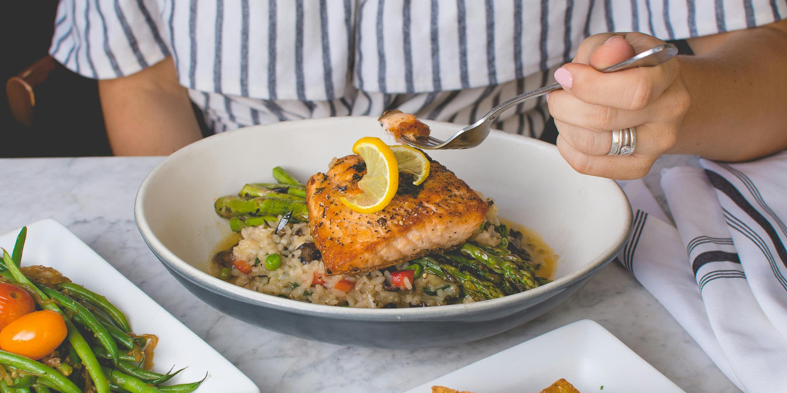 A person holds a fork over a plate of fish and vegetables.