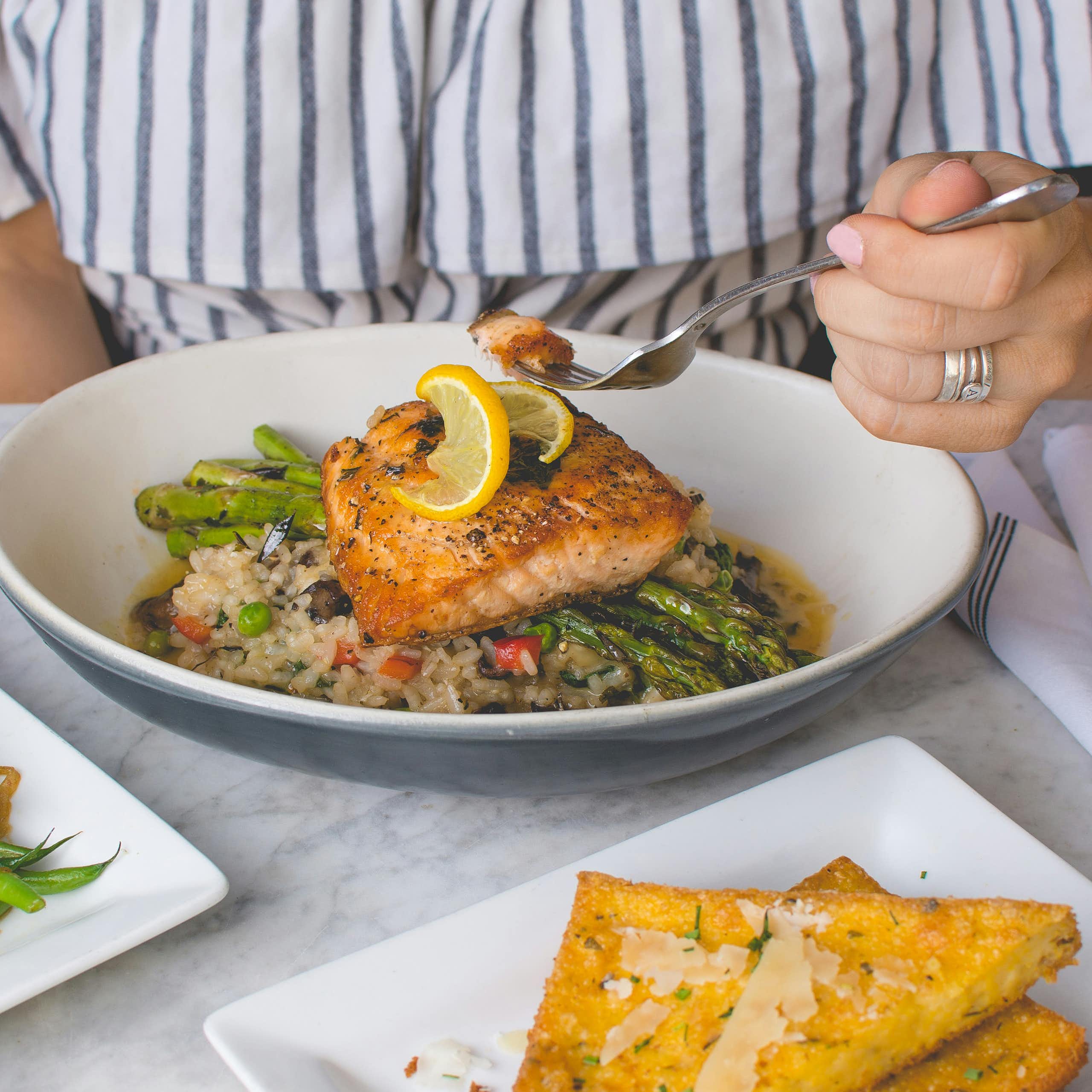 A person holds a fork over a plate of fish and vegetables.