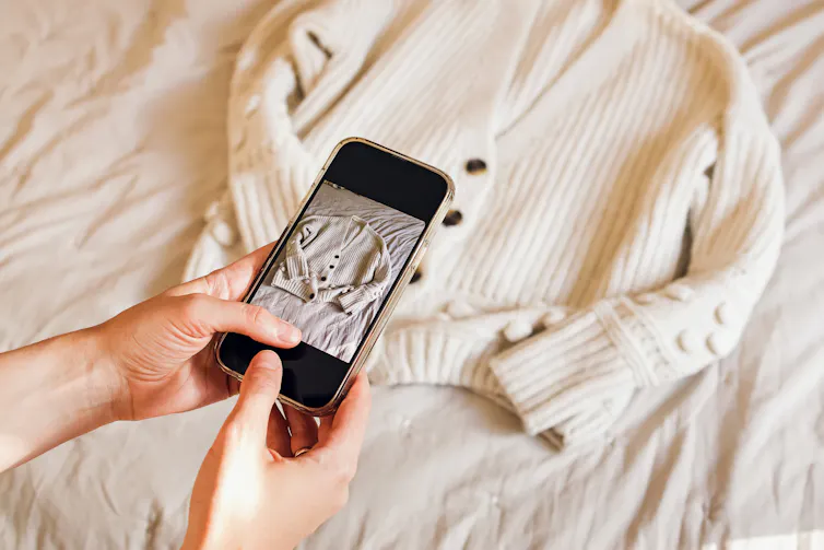 woman's hands holding phone taking photo of white jumper