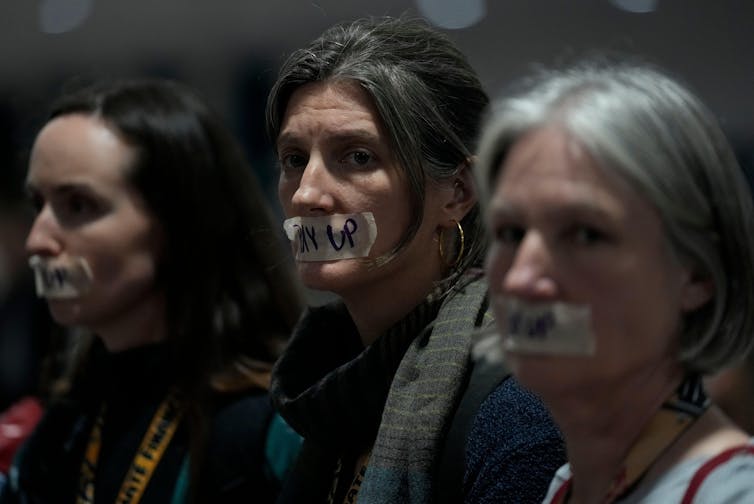 Three women with 'pay up' signs over their mouths