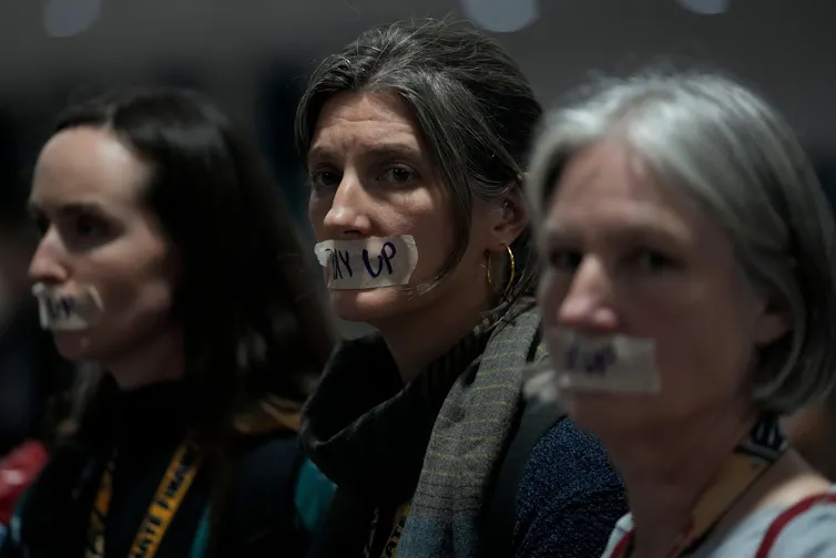 Three women with 'pay up' signs over their mouths