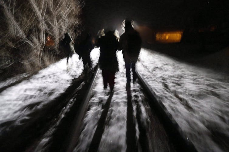 La verdad oculta sobre la muerte de los migrantes en la frontera en Canadá 2 Los migrantes en las siluetas se ven caminando una noche nevada a lo largo de los rastros del tren.