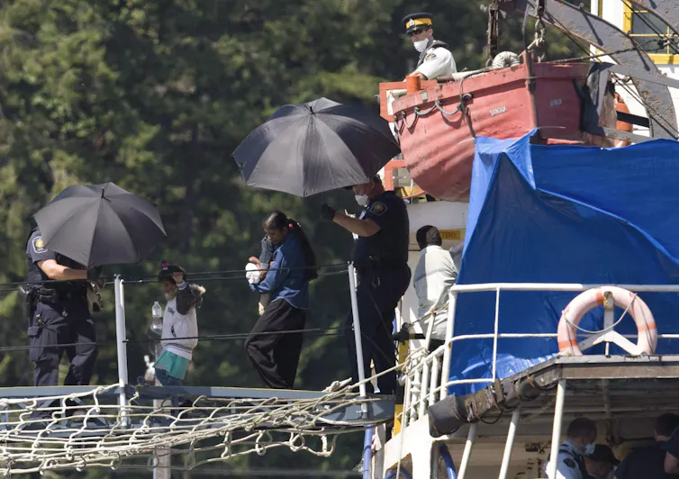 Migrants are shielded under black umbrellas as they disembark a boat.