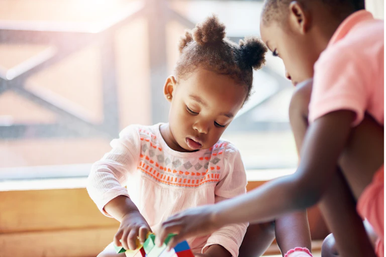 Une petite fille emboîtent des blocs de construction, en compagnie d'un enfant plus grand.
