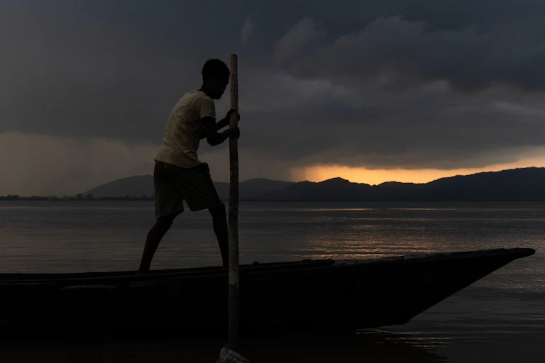 A fisherman sets out on a river under dark clouds.