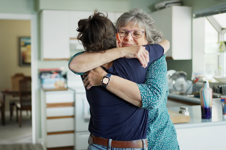 older woman hugs younger woman in kitchen
