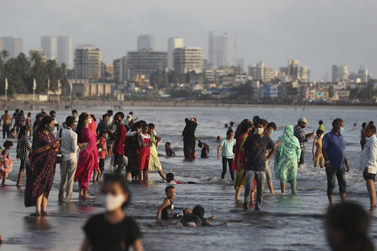 Dozens of people wade in water on a beach with tall buildings behind them.