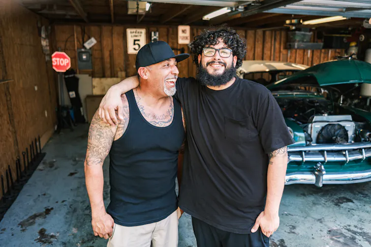 older man and younger man smiling and each with arm around the other
