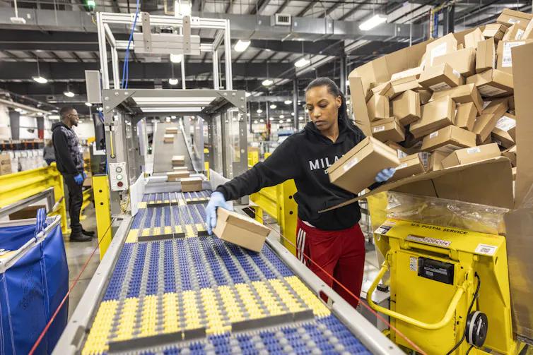 A Postal Service worker places packages on a parcel sorting machine.