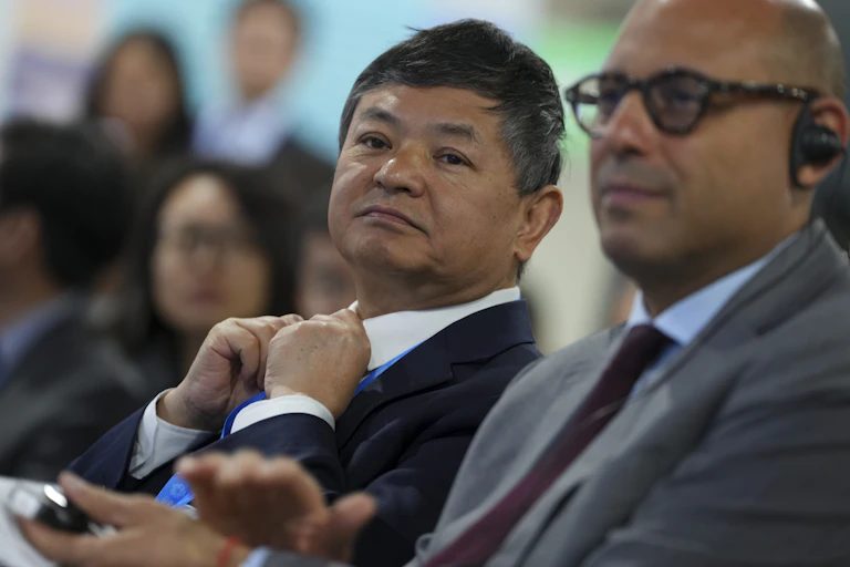 Two men, one Chinese and the other European, watch a speaker intently