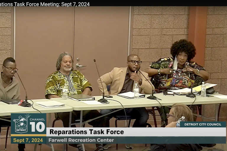 Four people sit behind stick microphones at a table.