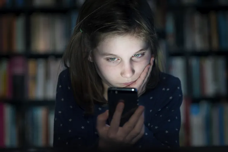 Girl in the dark looking sadly at a phone.