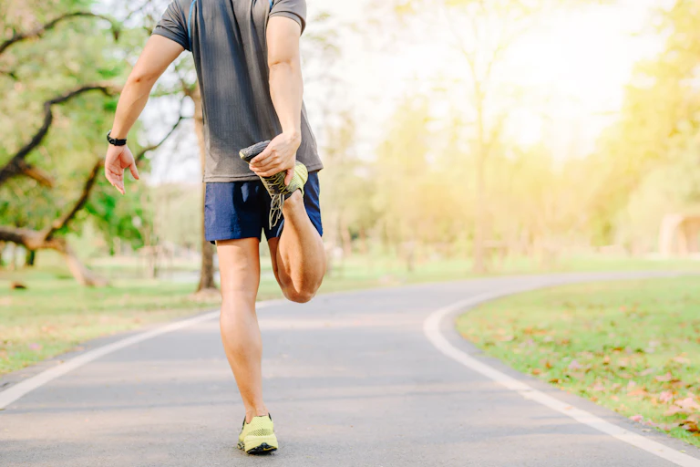 A man on a park track holding his foot in a stretch.