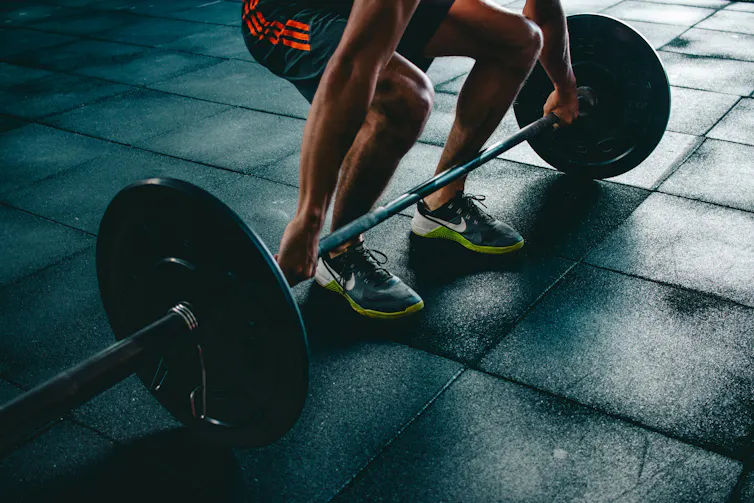 A man preparing to pick up a barbell in a gym.