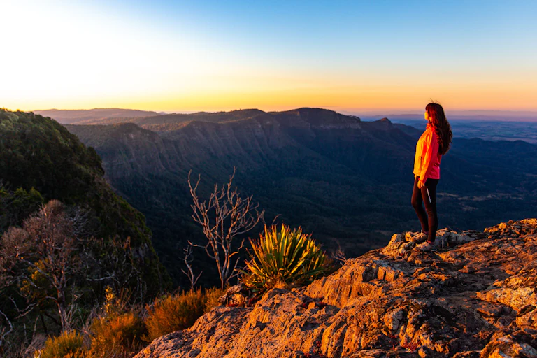 Female hiker looking out to the horizon over a mountain range at sunset