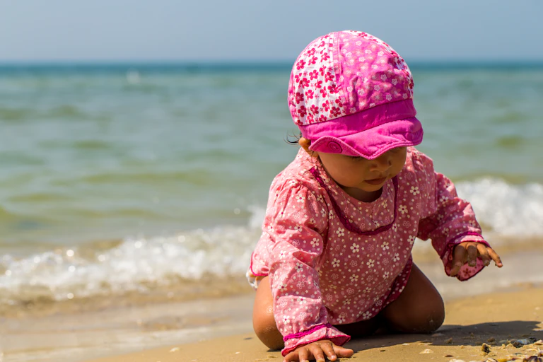 Baby crawling on a sunny beach, wearing a hat