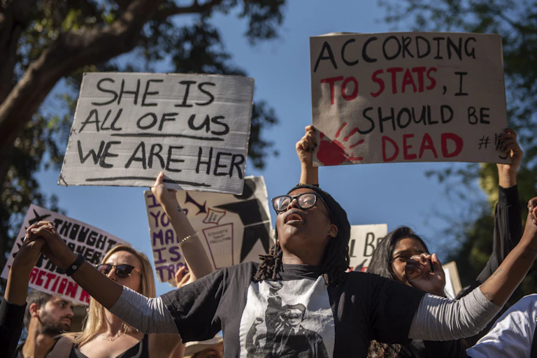 A group of protesters, some holding signs that read she is all of us we are her and according to stats I should be dead
