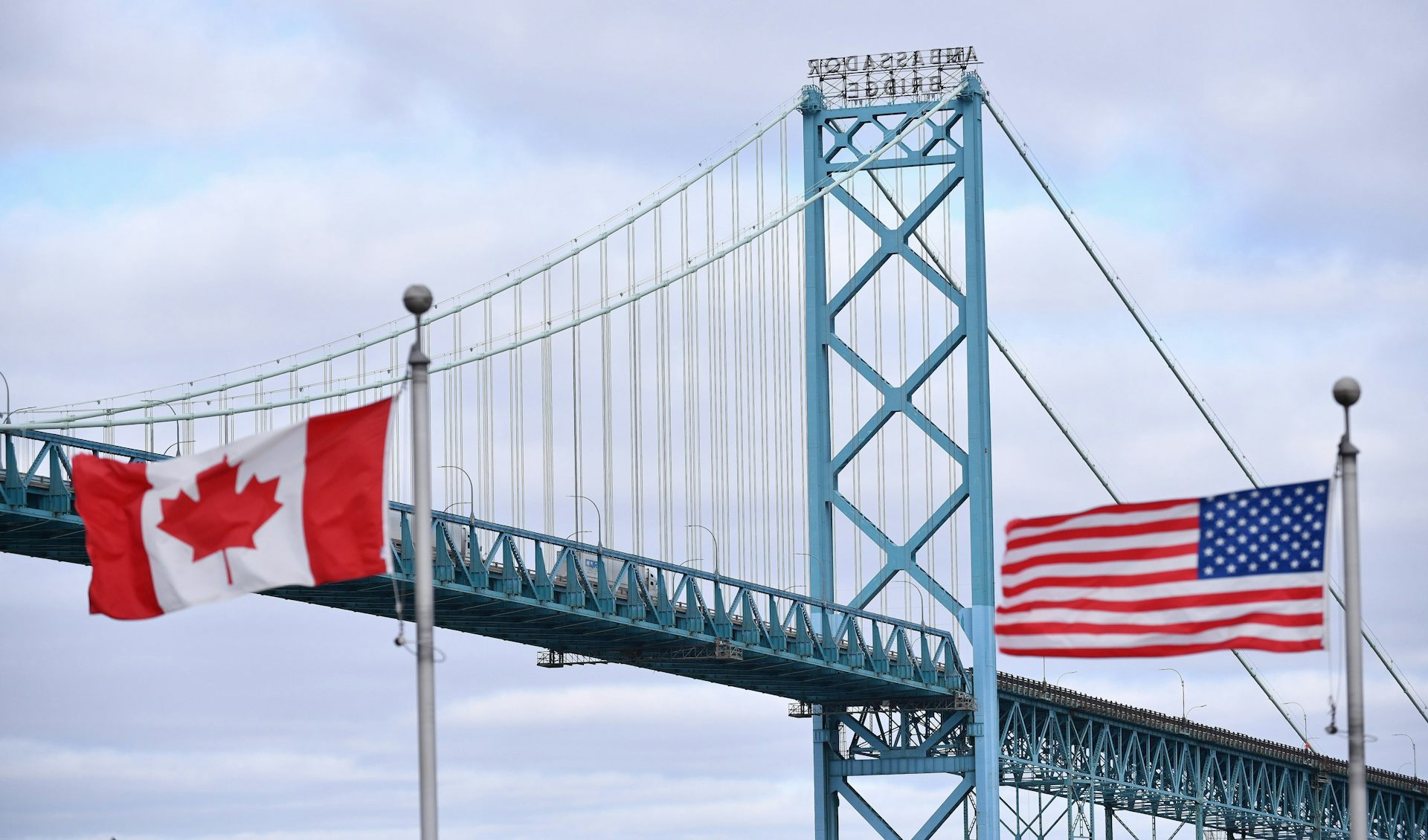 A suspension bridge with Canadian and U.S. flags in the foreground.