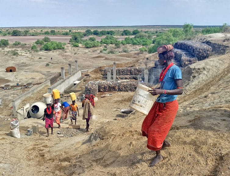 people carrying water buckets at a sandy construction site in open landscape