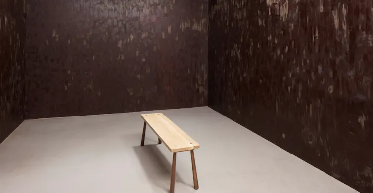 A wooden bench in a gallery space with walls painted in chocolate.