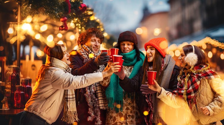 A group of young friends outdoors in a festive scene, clinking cups of hot liquid