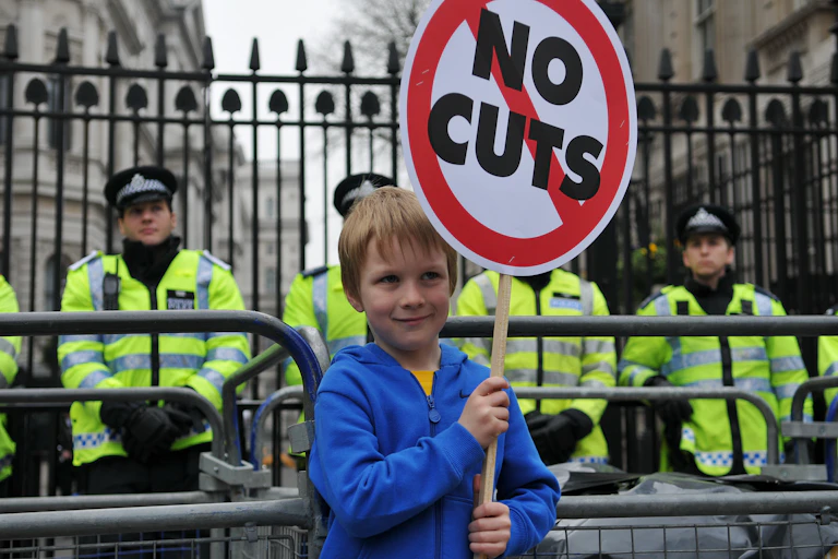 young boy protesting at downing street in london holding a sign saying no cuts
