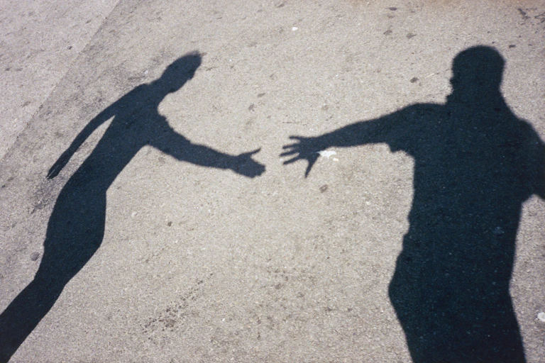 shadows of one person reaching a hand to another