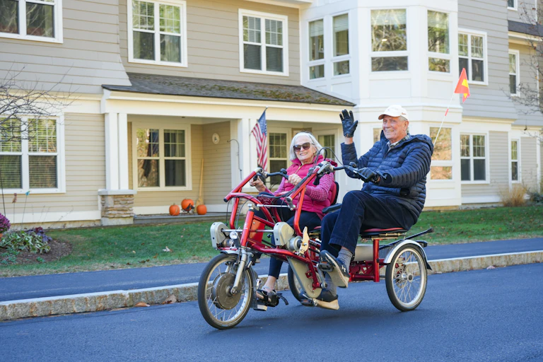 A man and woman ride past townhouses on a two-seat, three-wheeled cycle