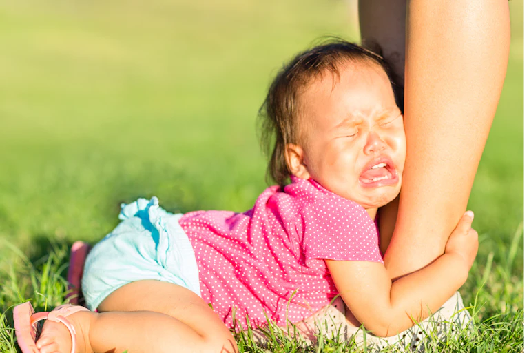 A child cries as they clutch their parent's leg.