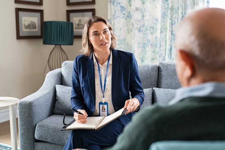 A female professional sitting on a couch talking to a man seated opposite.