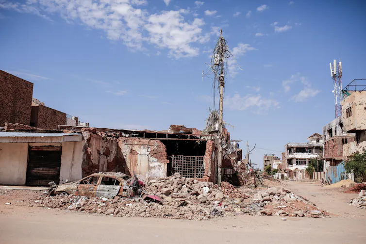 A burnt vehicle in front of a damaged shop in Sudan.