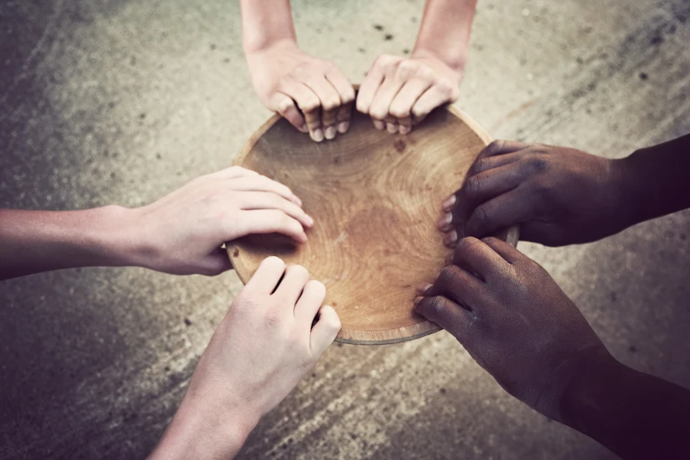 Three people holding onto an empty bowl.