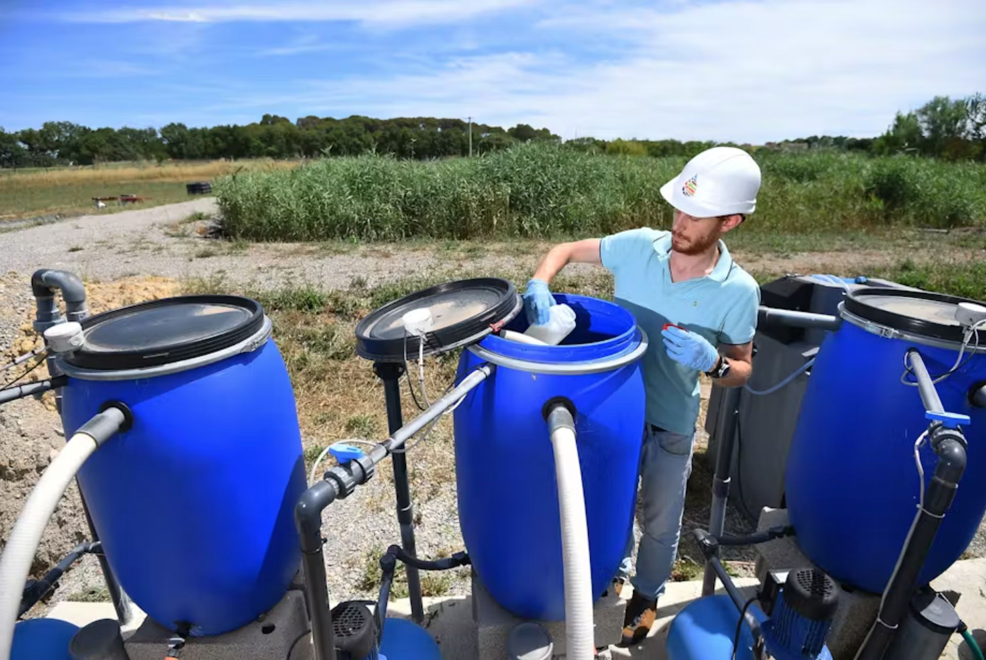 Un homme en casque travaille à vérifier la qualité de l’eau dans un tonneau en plastique