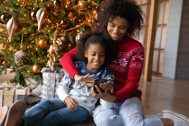 Mother and daughter looking at phone in front of Christmas tree