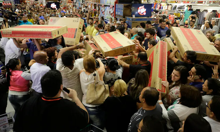 A crowd of shoppers reach for boxed televisions.