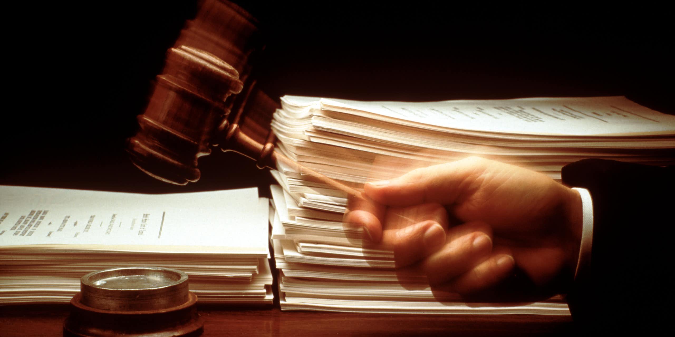 A hand swings a gavel down in front of large stacks of paper.