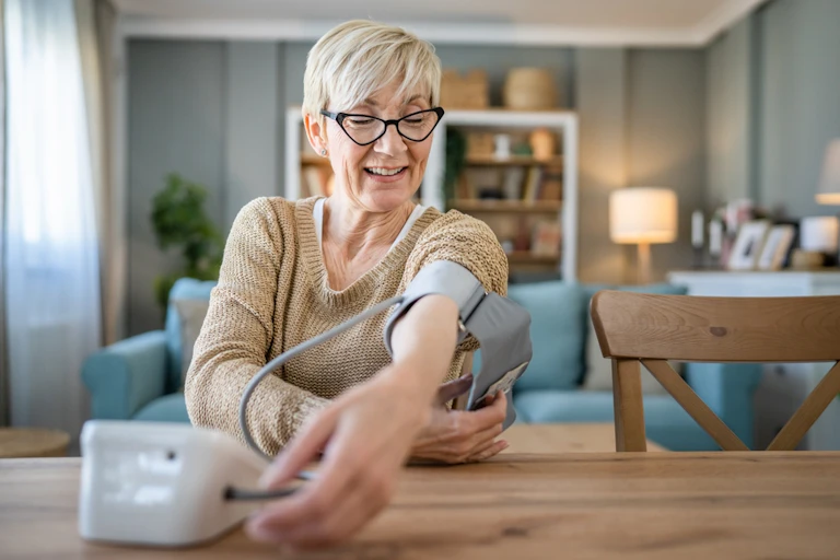 Woman sitting at table measuring blood pressure, cuff around upper arm
