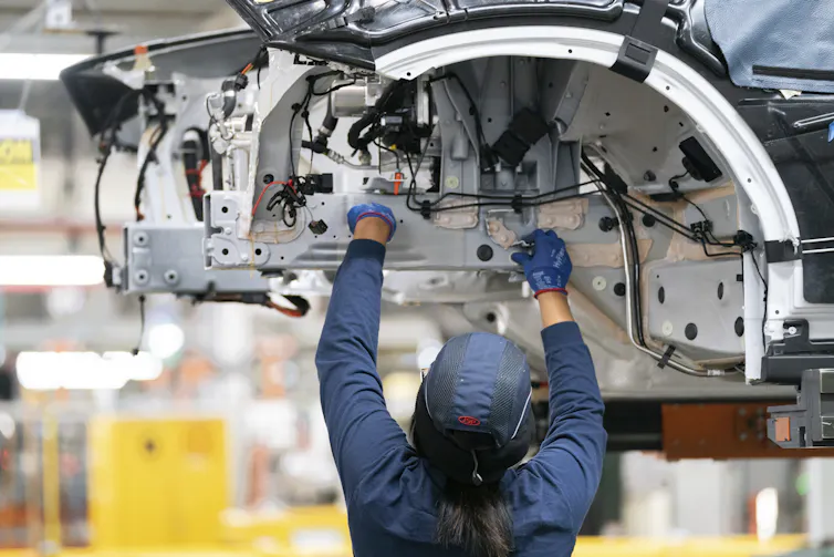 An employee works on a car on an assembly line