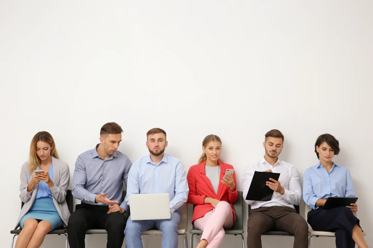 six jeunes assis sur des chaises devant un mur blanc.. ils paraissent attendre