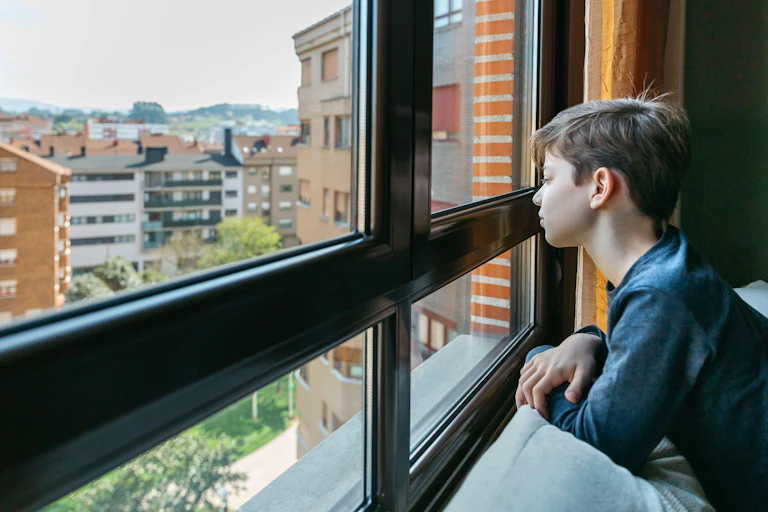 A teenager stares out of an apartment window.