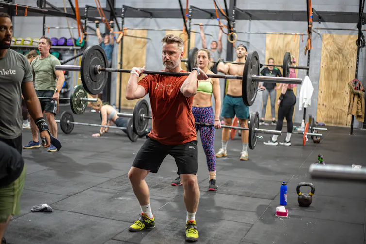 A middle aged man performs CrossFit in a gym with others.