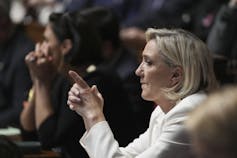 A woman seen in silhouette with blonde hair with her hands clasped and index fingers extended.